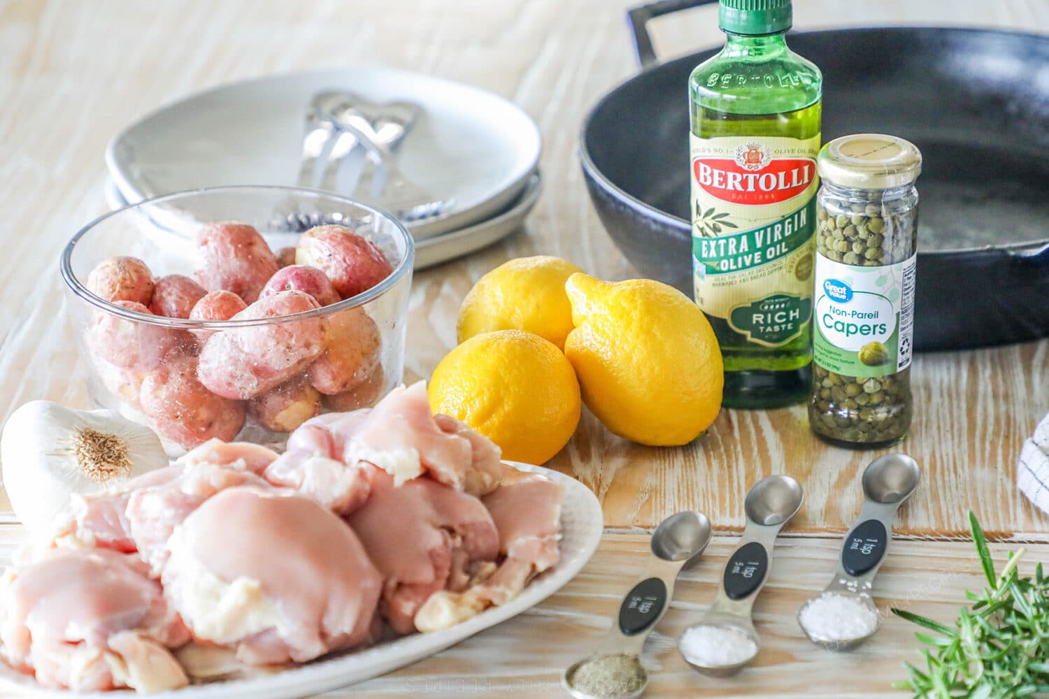 Ingredients needed to make baked lemon chicken thighs with potatoes on a wooden background.
