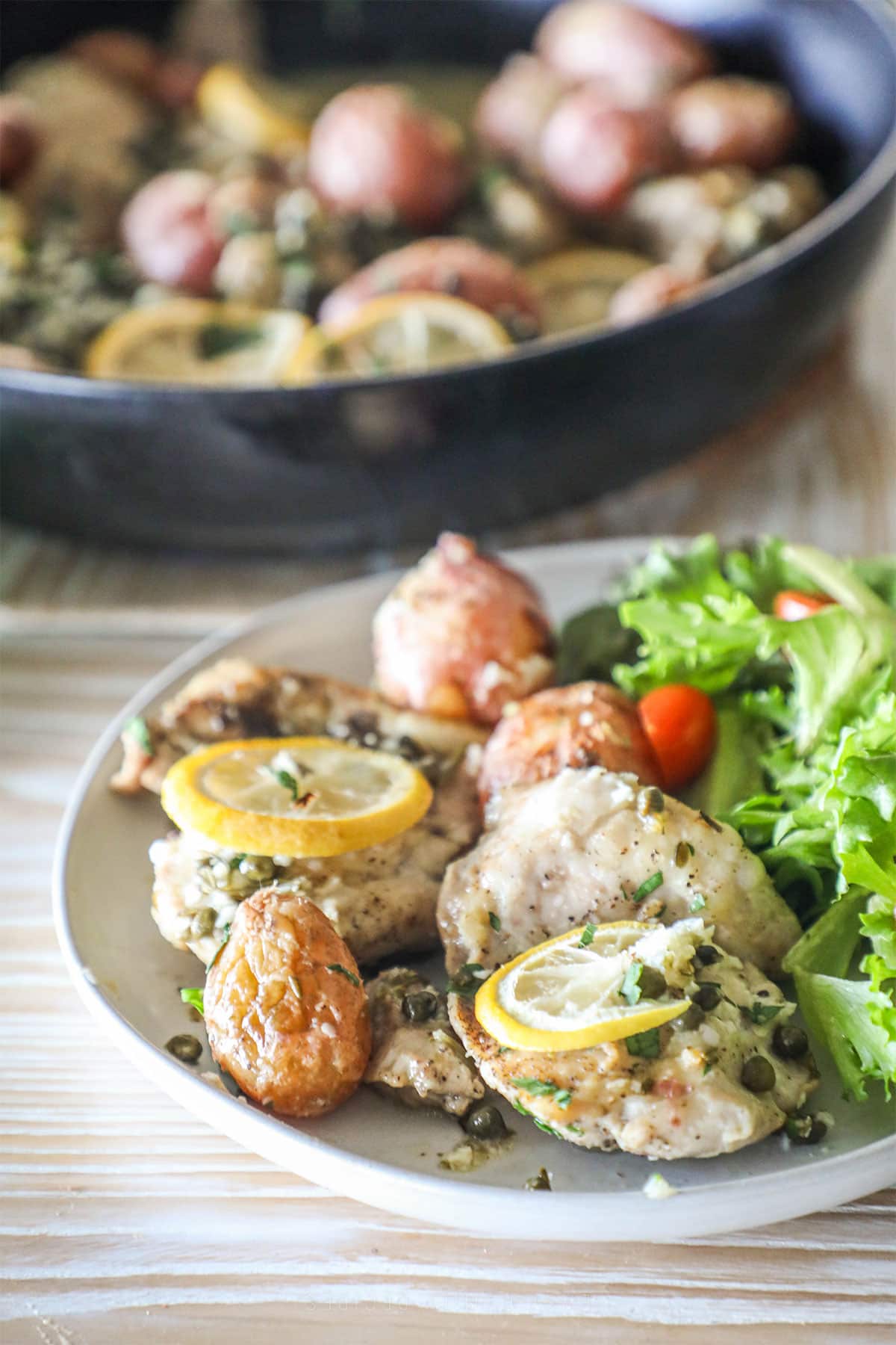 Baked lemon chicken thighs with potatoes on a plate with a green salad.