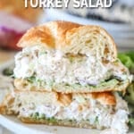 two halves of a croissant turkey salad sandwich stacked on a plate.