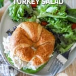 above image of a croissant turkey salad sandwich on a plate with a side salad.
