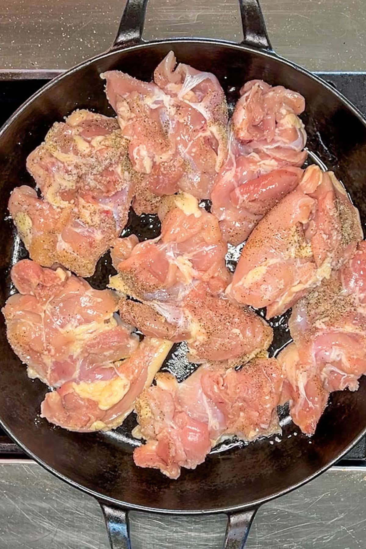 Chicken thighs searing in a hot cast iron skillet.