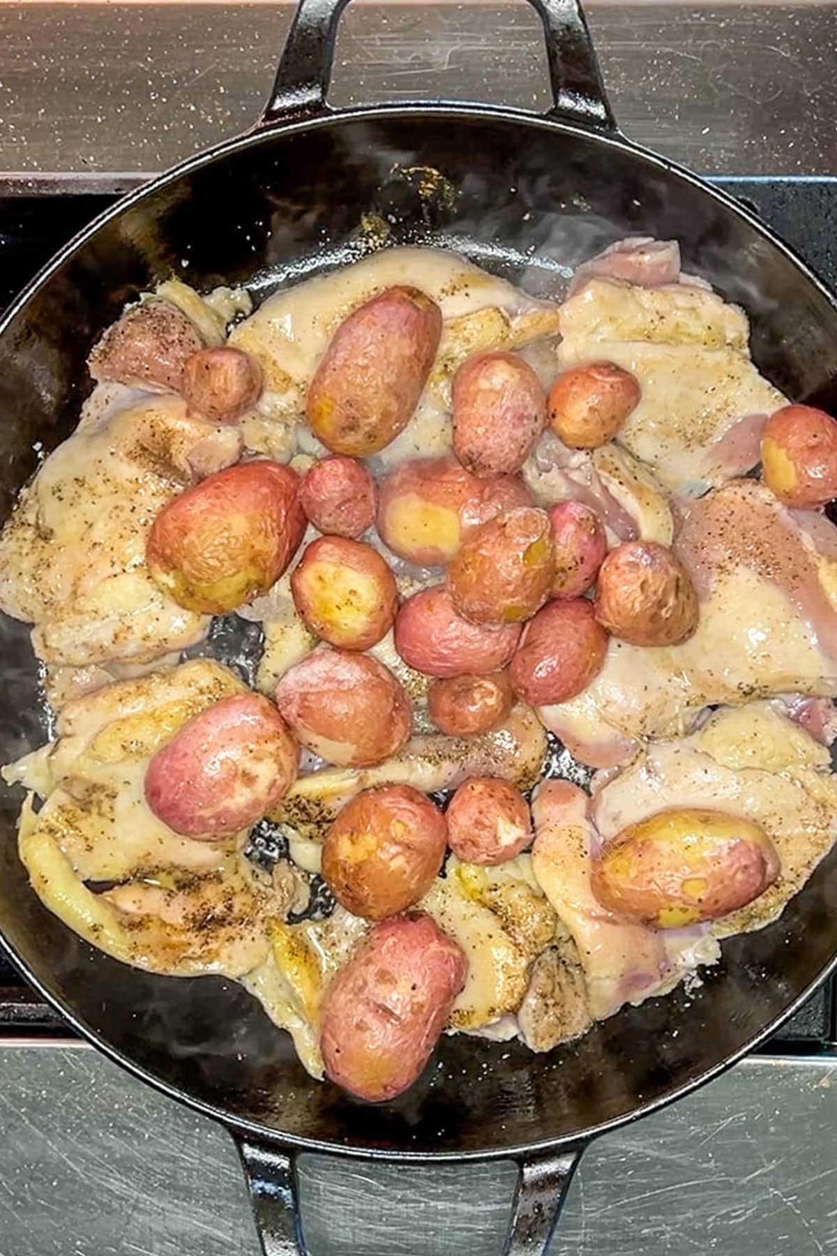 Potatoes added to the chicken thighs in a cast iron skillet.