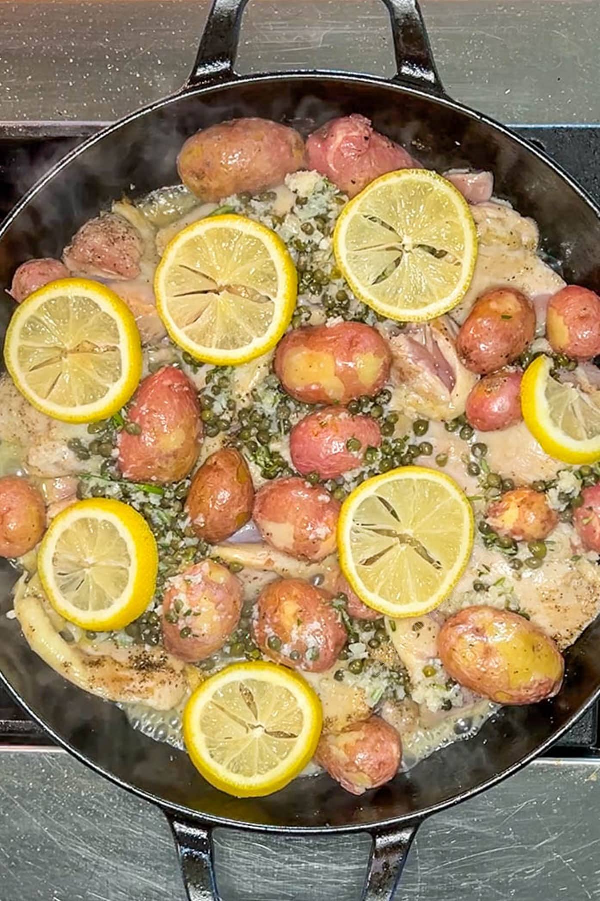 Lemon caper sauce and lemon slices placed on top of chicken and potatoes.