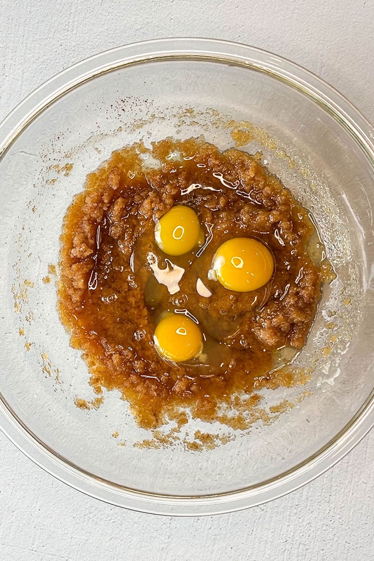 glass bowl of brown butter and creamed ingredients with 3 eggs on top