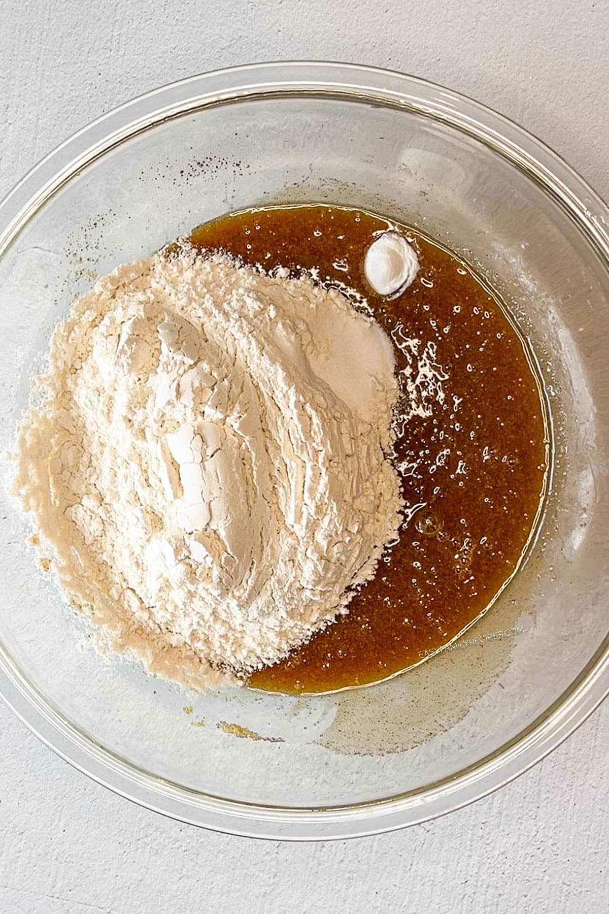 glass bowl of browned butter and other creamed ingredients with dry ingredients poured on top