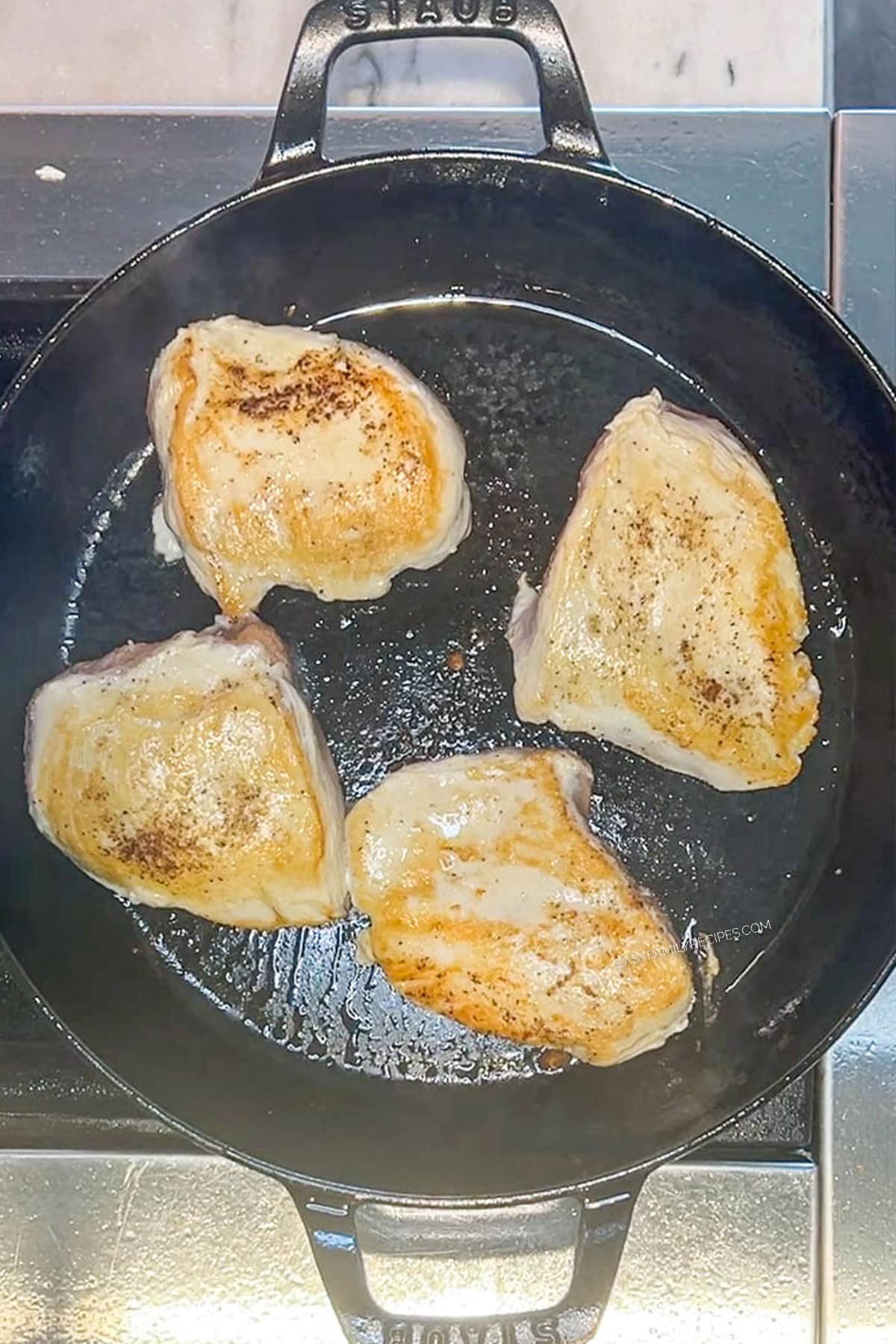 Chicken thighs searing in a large cast iron skillet.