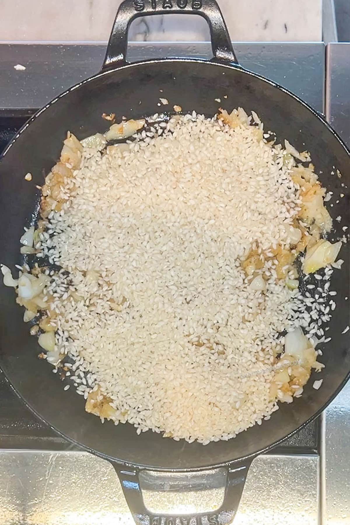 Risotto rice added to the sautéed onions and garlic in a skillet.