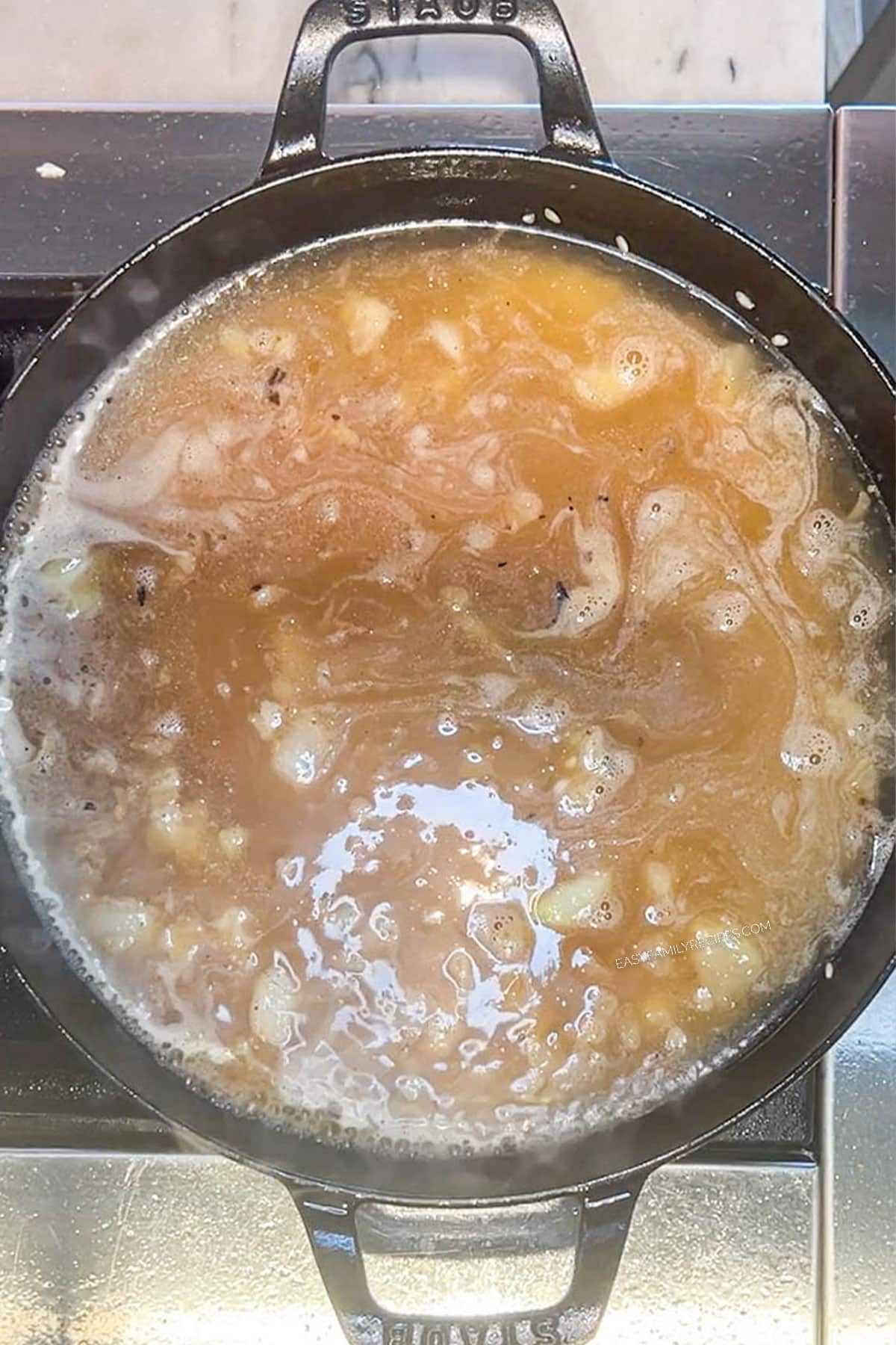Broth added to the rice and onions in a skillet.