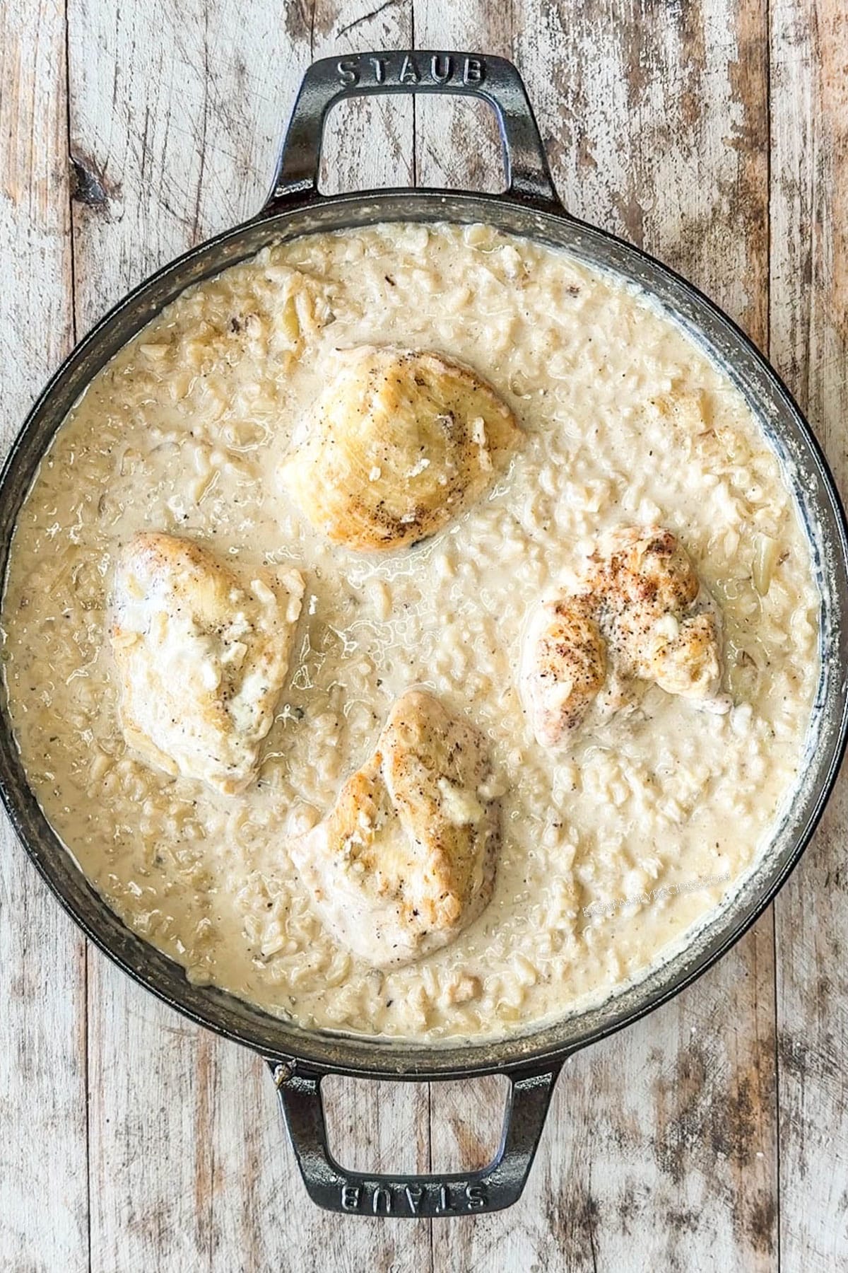 Chicken thighs with cooked Boursin risotto in a cast iron skillet.