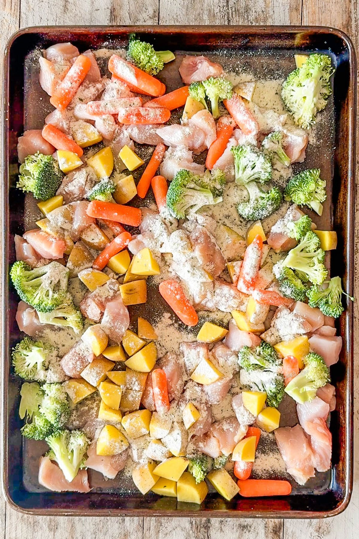 raw chicken and veggies on a sheet pan topped with ranch seasoning.