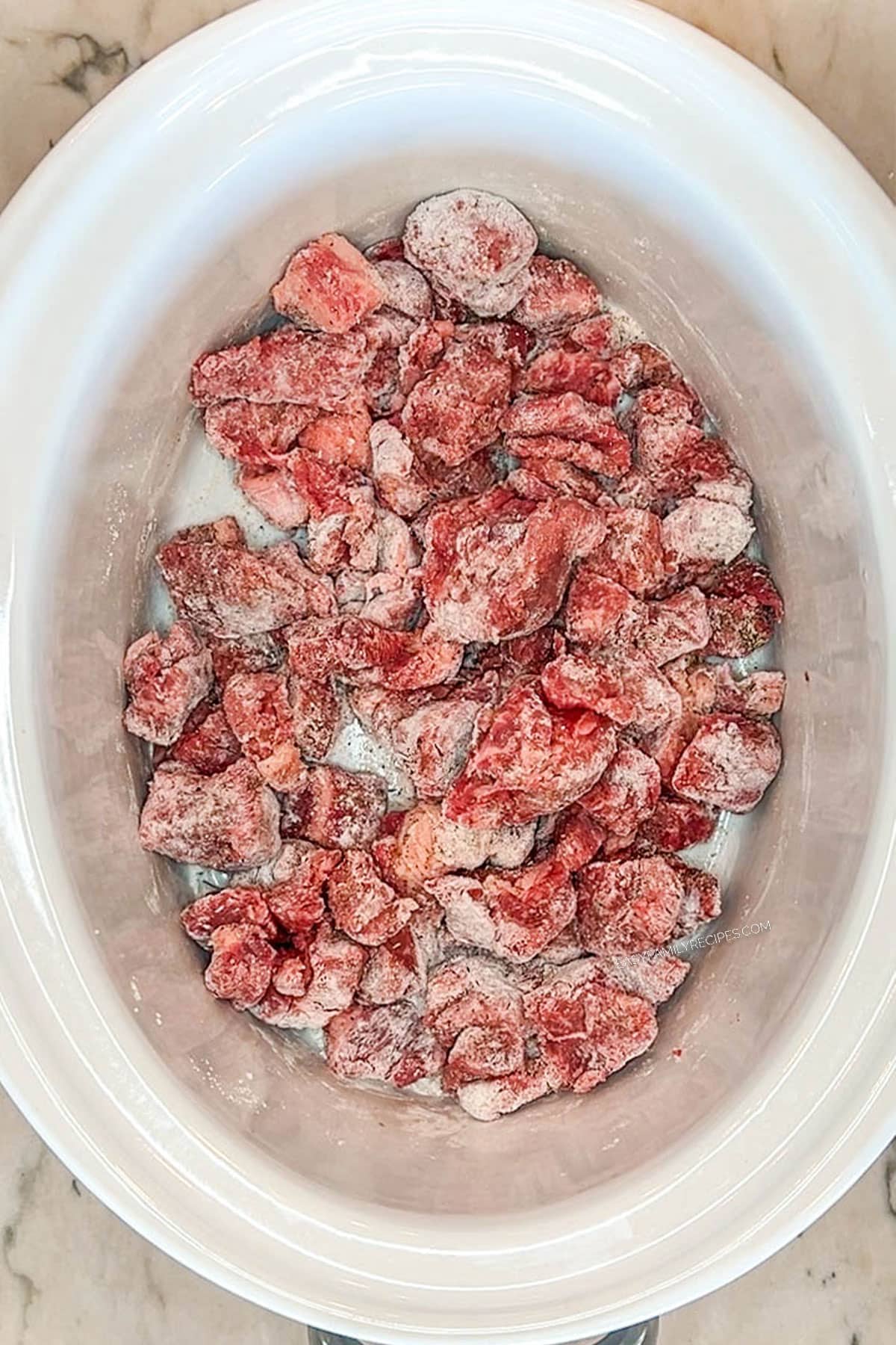 stew meat tossed in seasonings in bottom of white crock pot