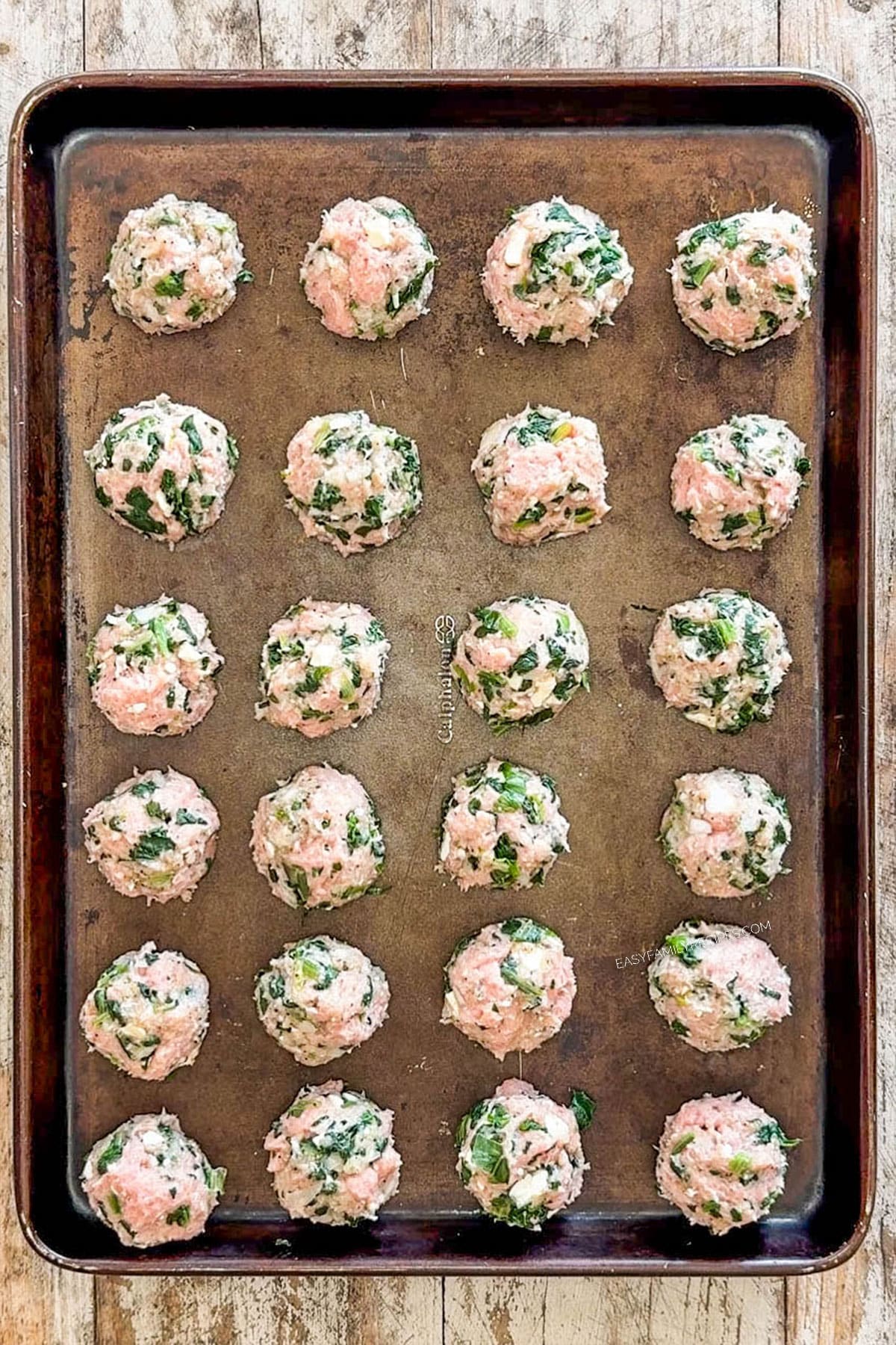 Assembled Greek meatballs lined up on a sheet pan before being baked.
