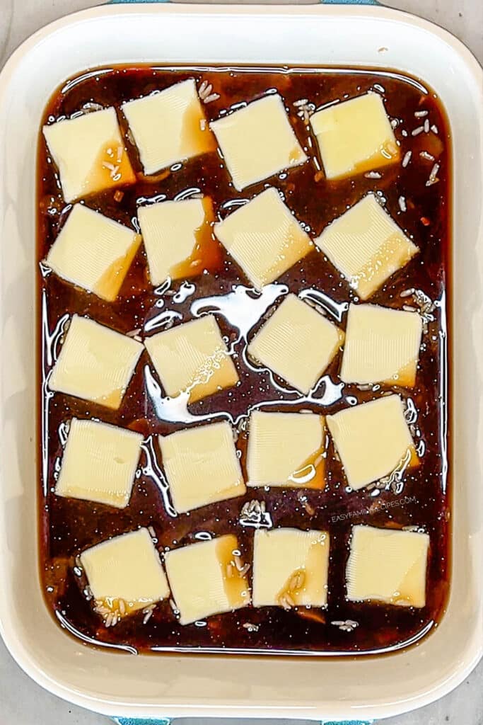 rice, beef broth, and soup in a baking dish topped with pats of butter.