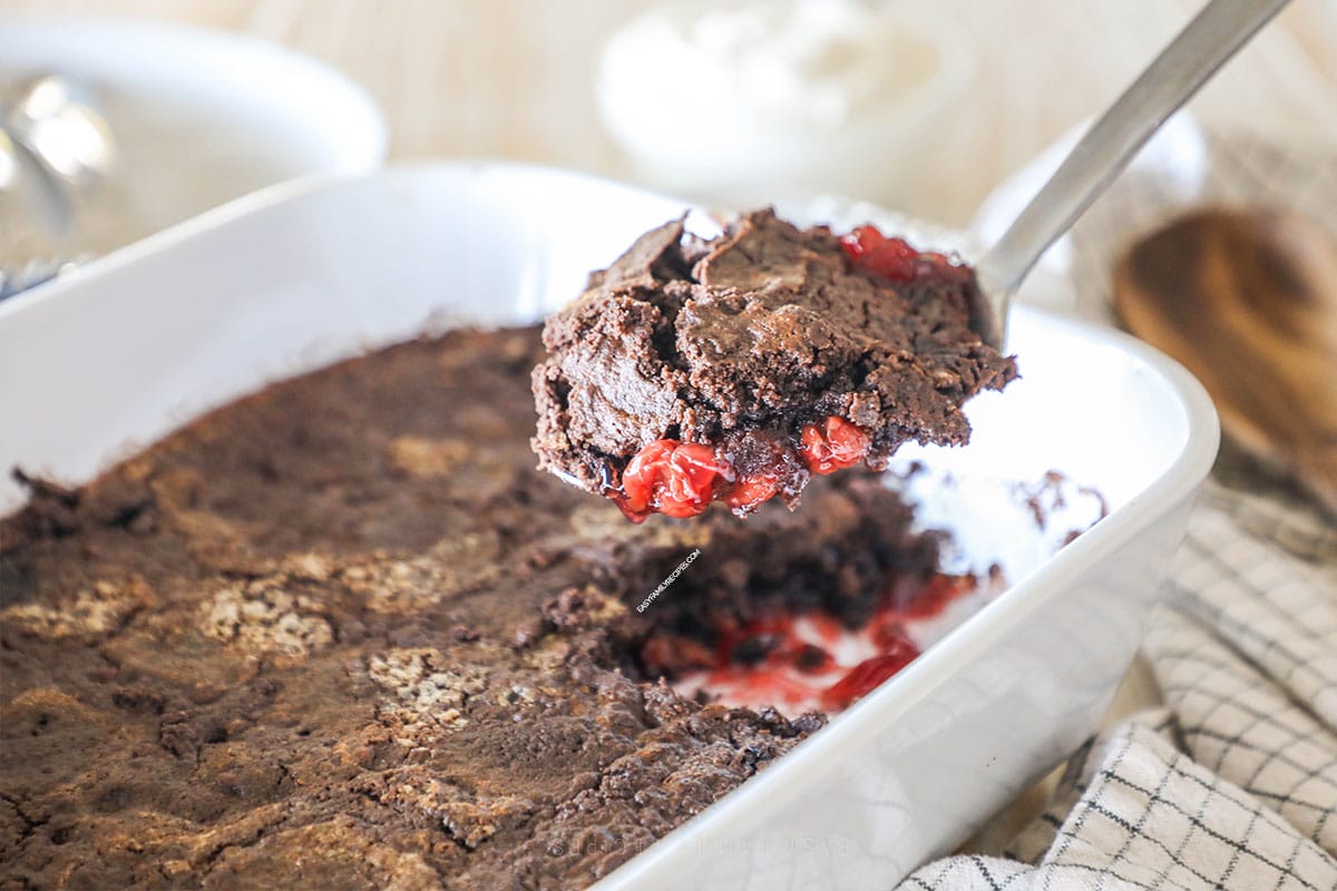 a scoop of black forest dump cake being scooped out of a baking dish. 