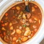 Slow cooker beef stew in a white crockpot with a wooden spoon stirring