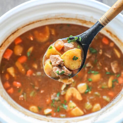 white crock pot with beef stew and wooden spoon coming out