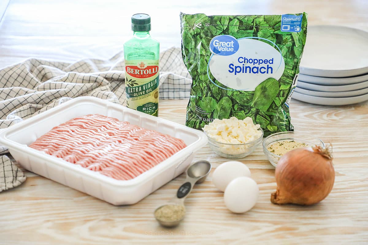Ingredients needed to make spinach feta turkey meatballs on a wooden background.