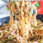 Tongs swirling up some garlic pork peanut noodles from a pan.