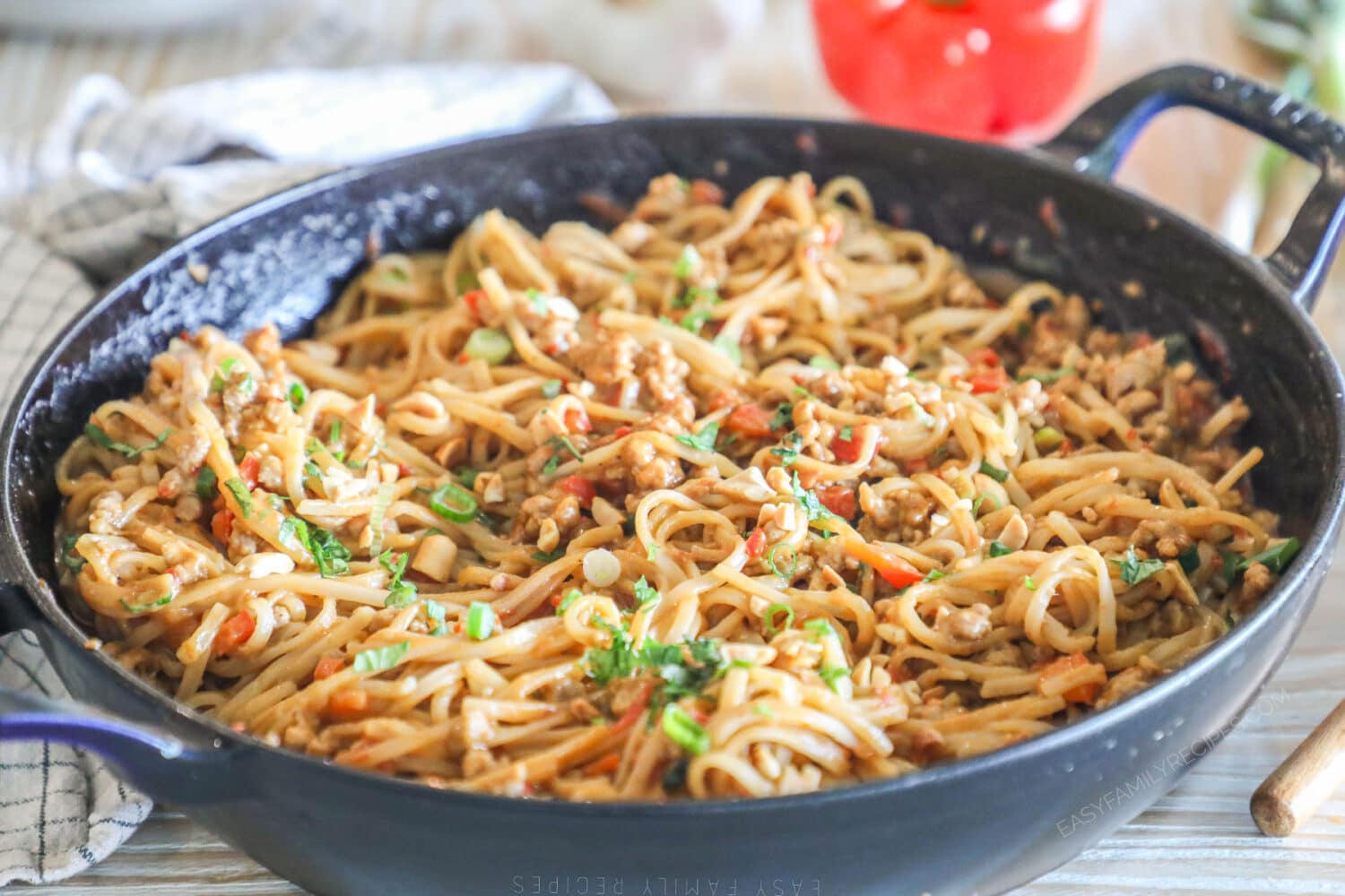 Side view of garlic pork peanut noodles in a cast iron skillet garnished with green onions.