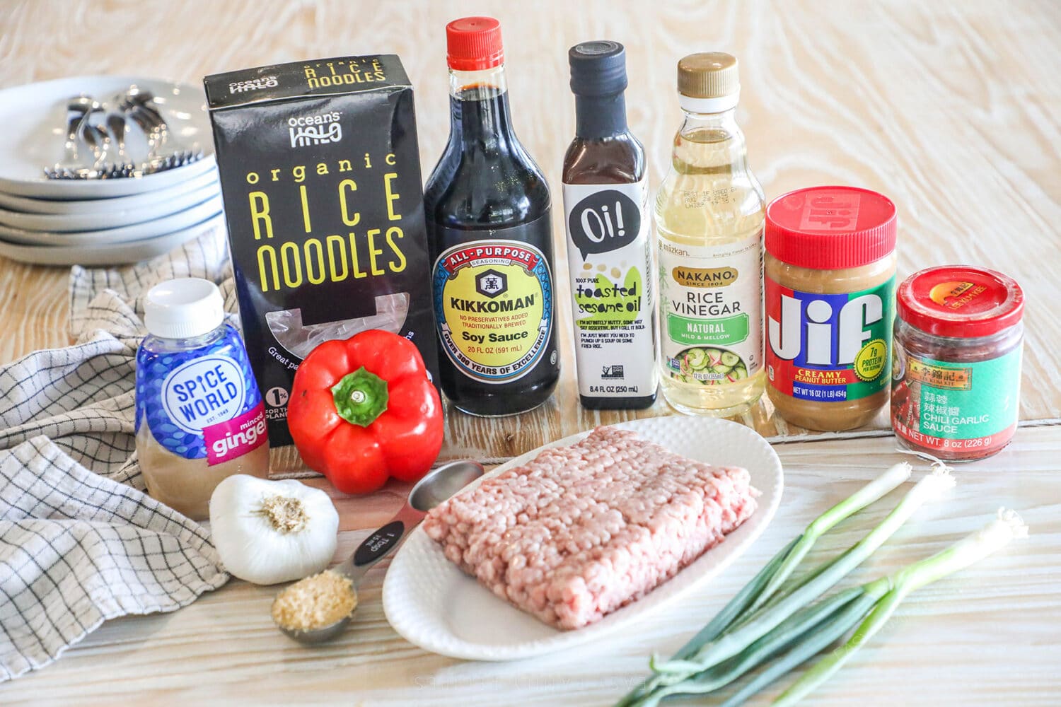 Ingredients needed to make garlic pork peanut noodles on a wooden background.