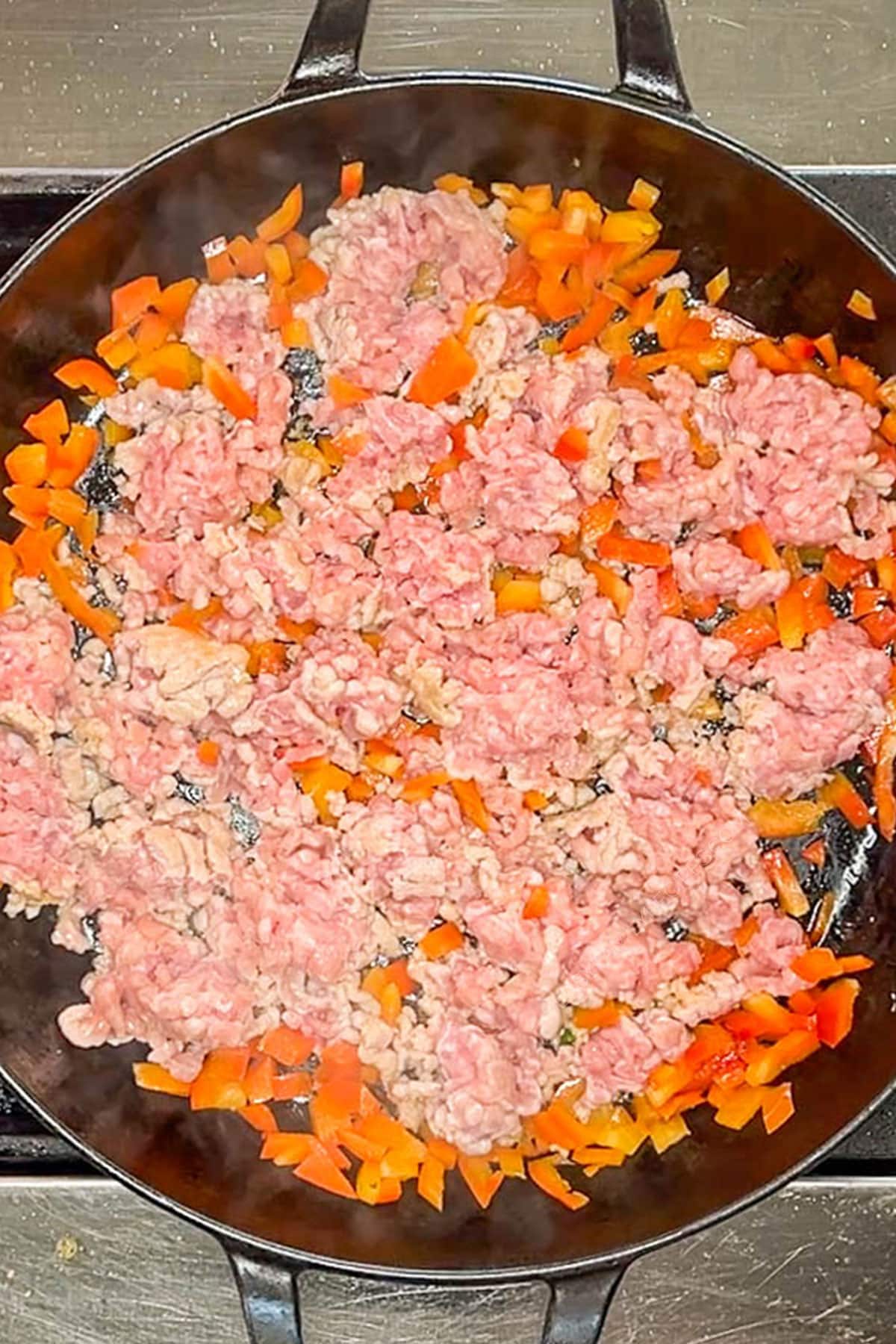 Ground pork getting browned in a skillet with bell peppers.