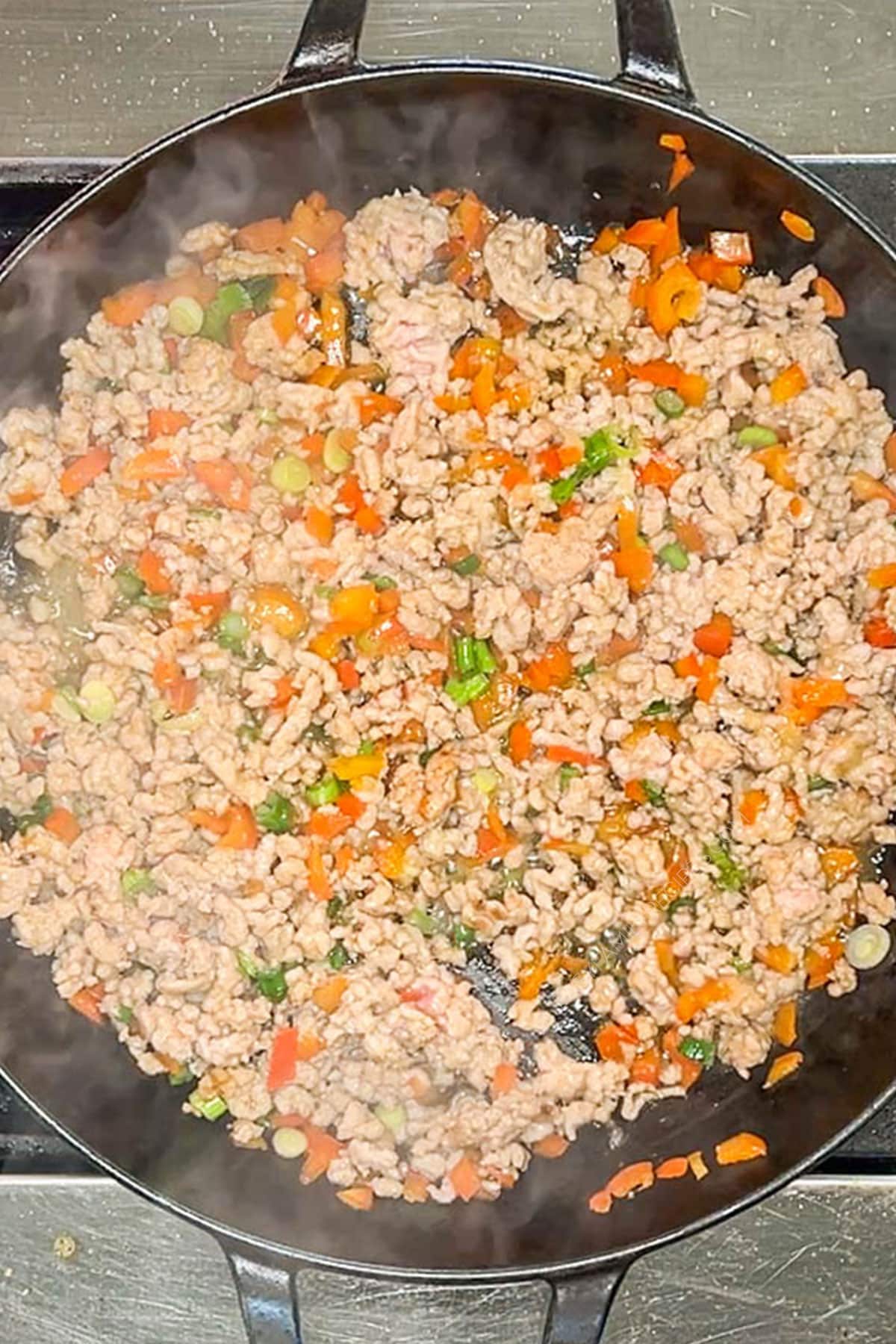 Browned ground pork in a skillet with bell peppers and green onions.