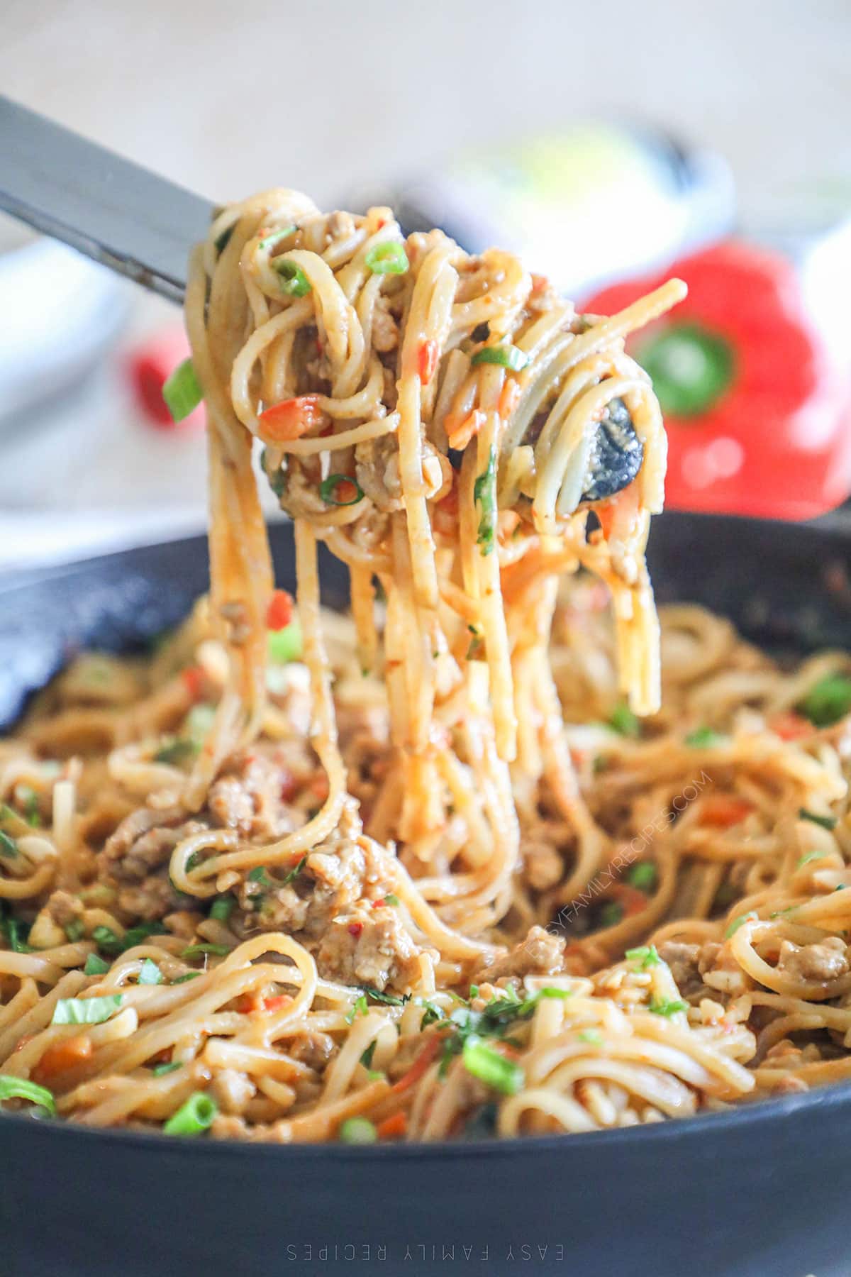 Tongs swirling up the garlic pork peanut noodles from the skillet.