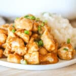 Side view of oven baked orange chicken on a plate garnished with green onions.