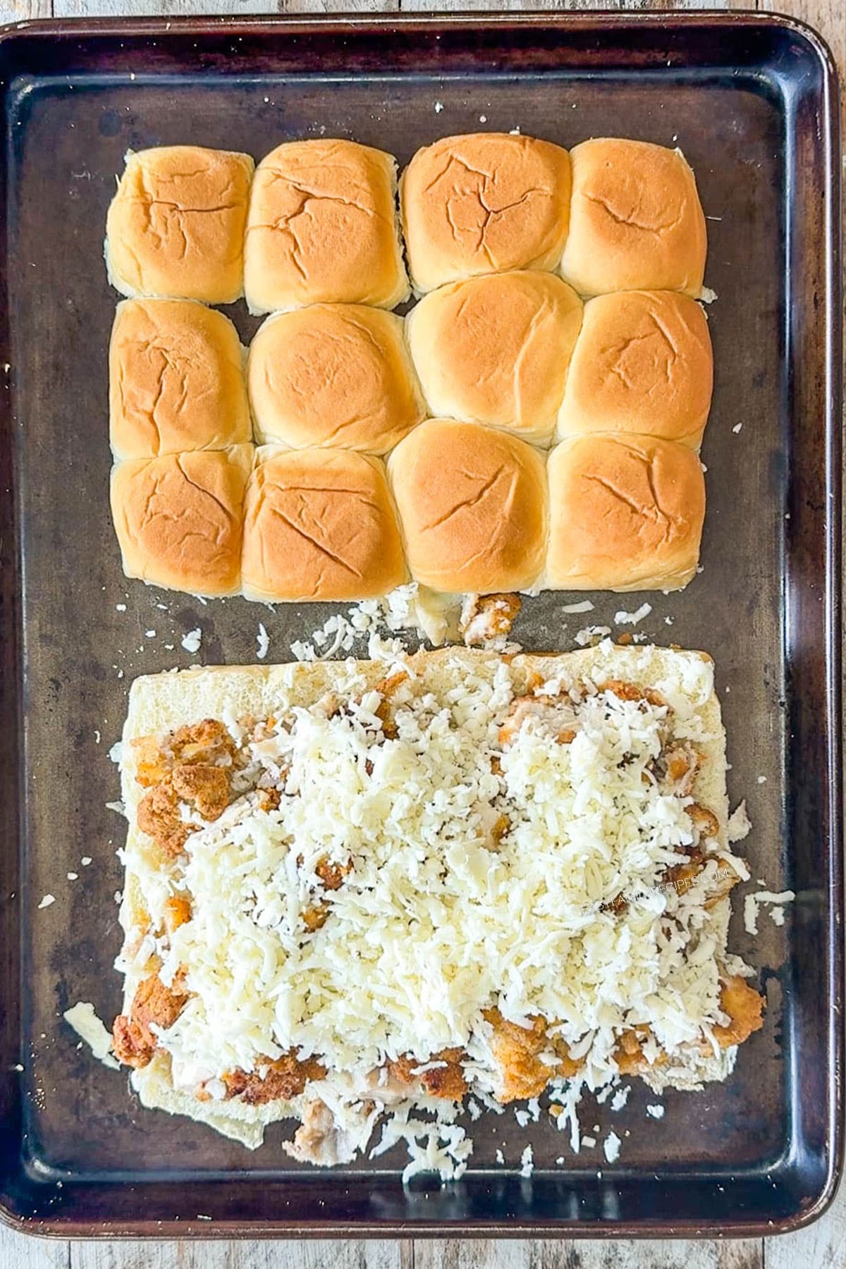 Split the rolls in half and place on a sheet pan. Then, add the chopped crispy chicken on the bottom half of the buns and top with the shredded cheese. Keep the top cut side down on the pan.