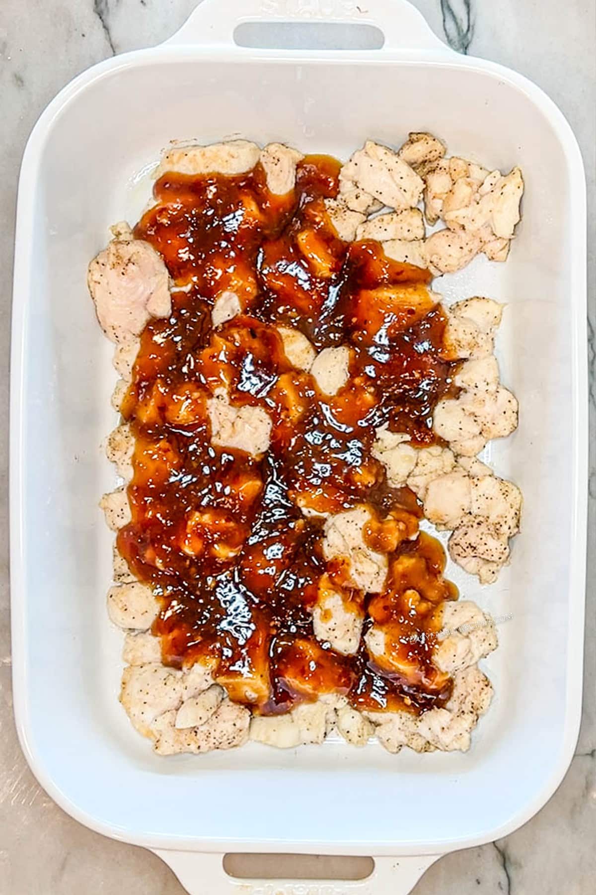 Chicken in a baking dish with sauce poured over the top.
