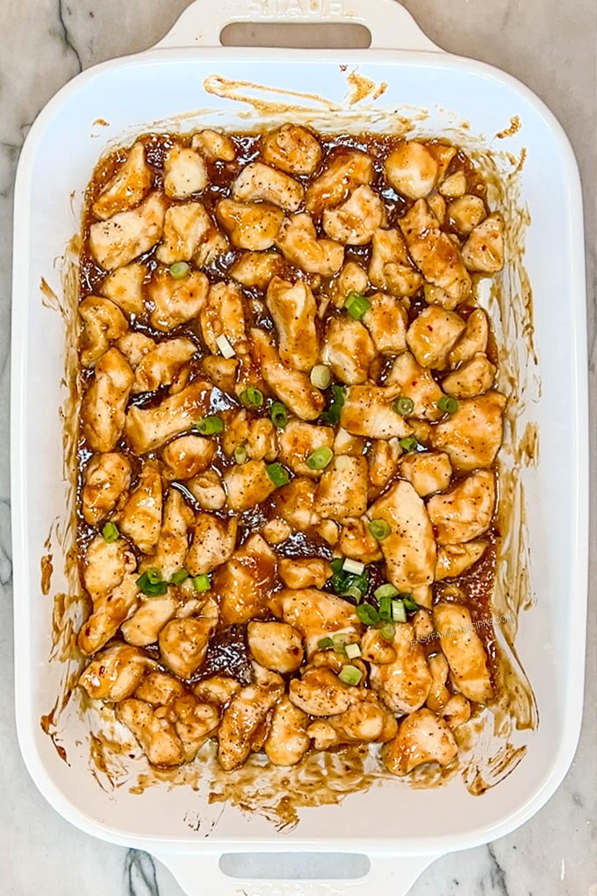 Oven baked orange chicken in a white baking dish after baking.