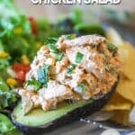 mexican chicken salad piled on an avocado half, served with a side salad and tortilla chips.