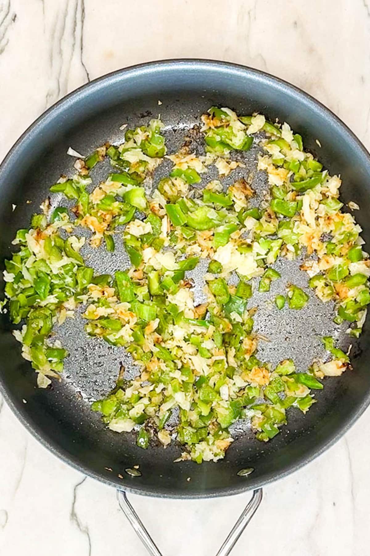Onions and green bell pepper sautéing in a skillet.
