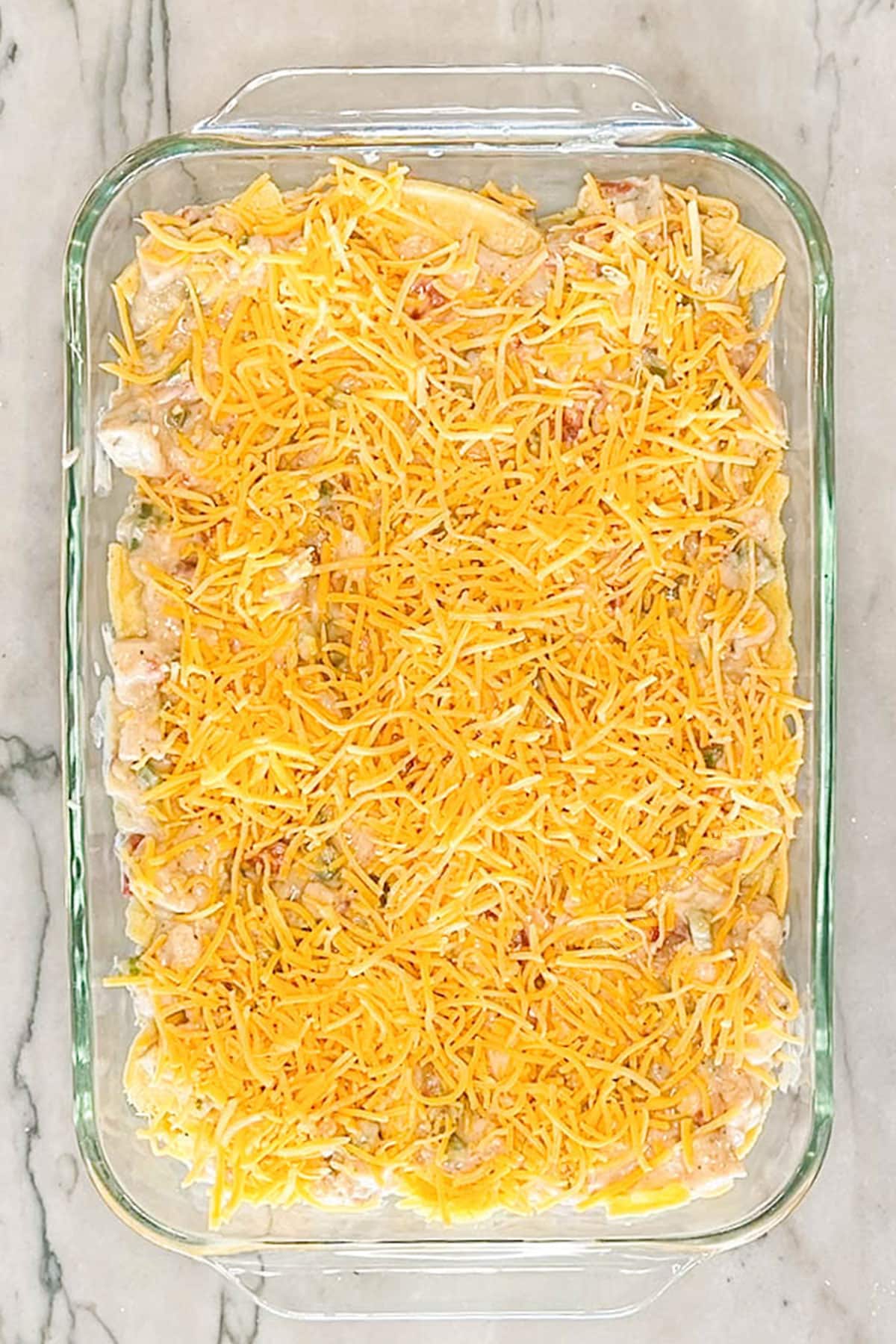 Shredded cheese on top of assembled king ranch chicken casserole before baking.