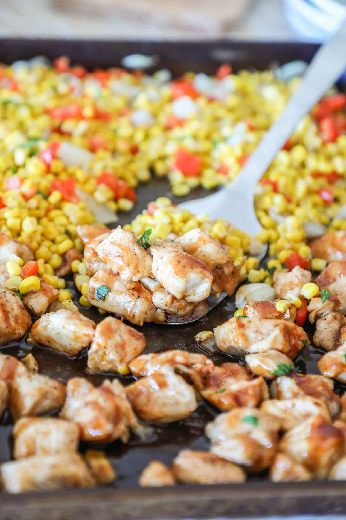 Spatula scooping up some chicken and buttered corn on a sheet pan.