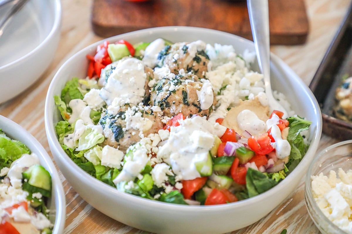 Mediterranean meatball bowl with rice, meatballs, salad and tzatziki on top.