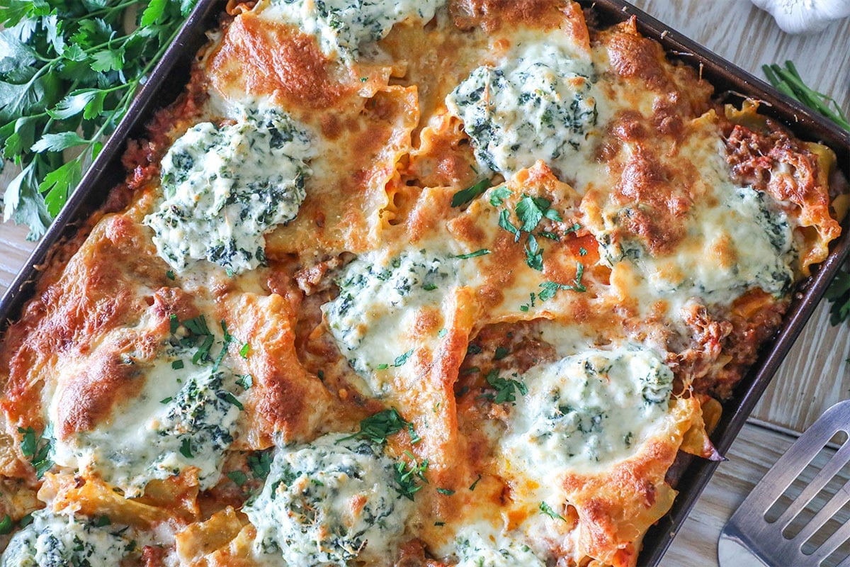 Baked sheet pan lasagna after cooking. On a wooden table with fresh herbs.