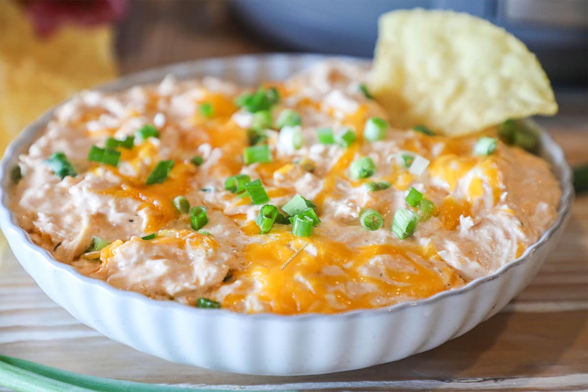 a serving dish filled with cheesy buffalo chicken dip and garnished with green onions.
