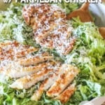 crispy parmesan chicken breasts sliced and placed over green goddess salad in a large white bowl with two wooden spoons- on a wooden background