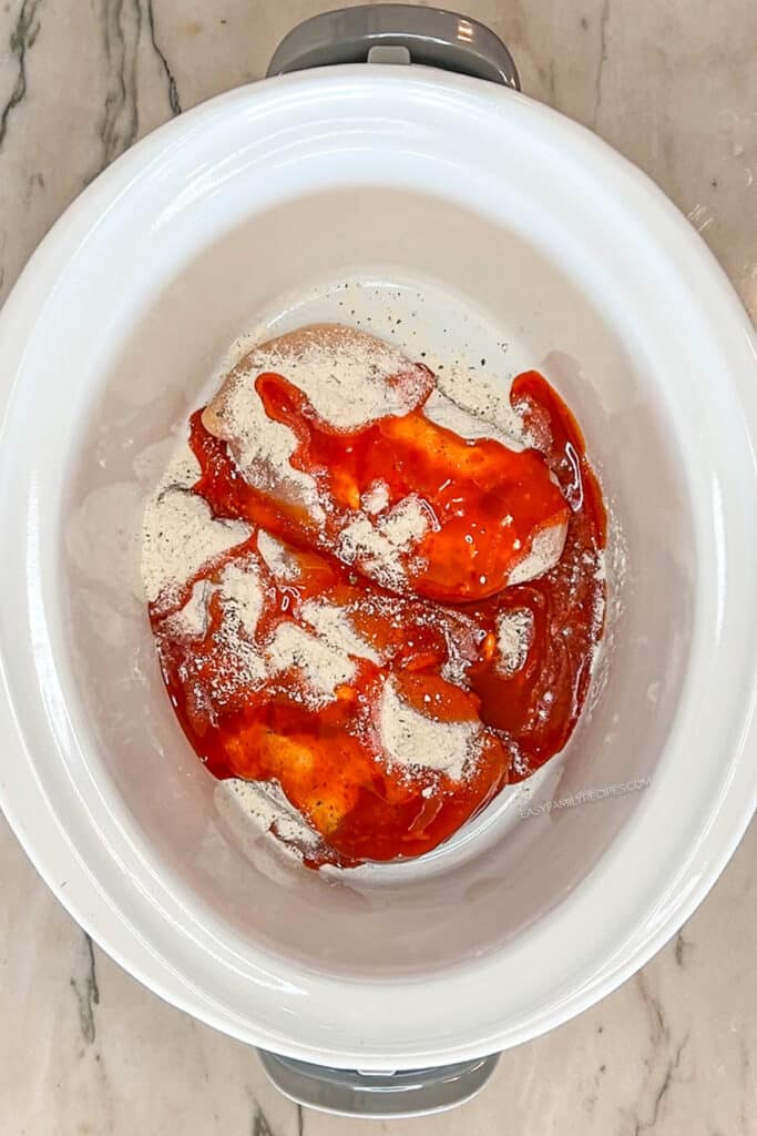 chicken breasts in a crockpot topped with buffalo sauce and ranch seasoning.