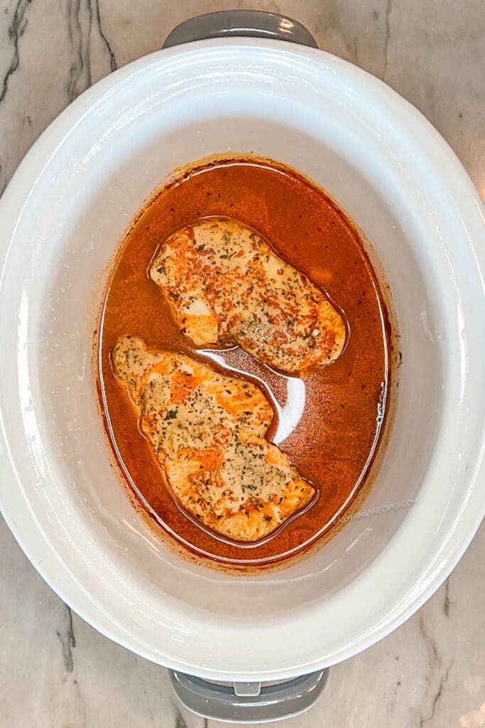 cooked chicken breasts in a crockpot with buffalo sauce.