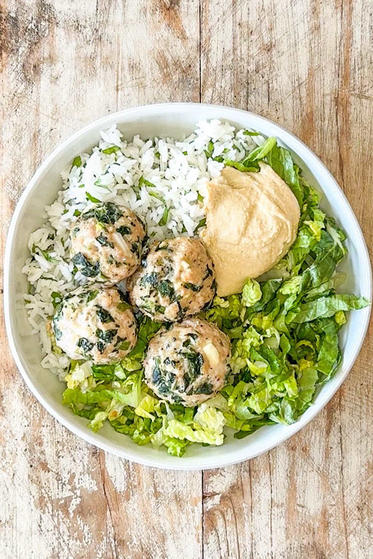 Rice, lettuce, meatballs and hummus placed in a white bowl.