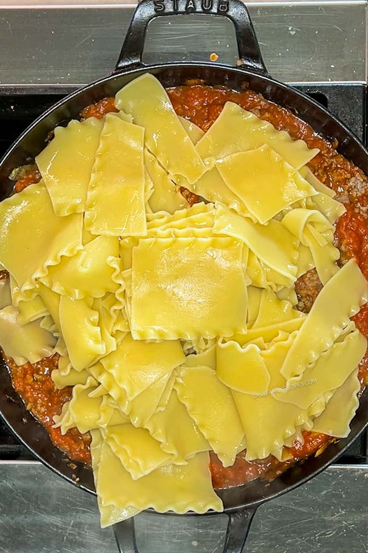 Skillet containing ground beef and marinara sauce with cooked, broken lasagna noodles on top