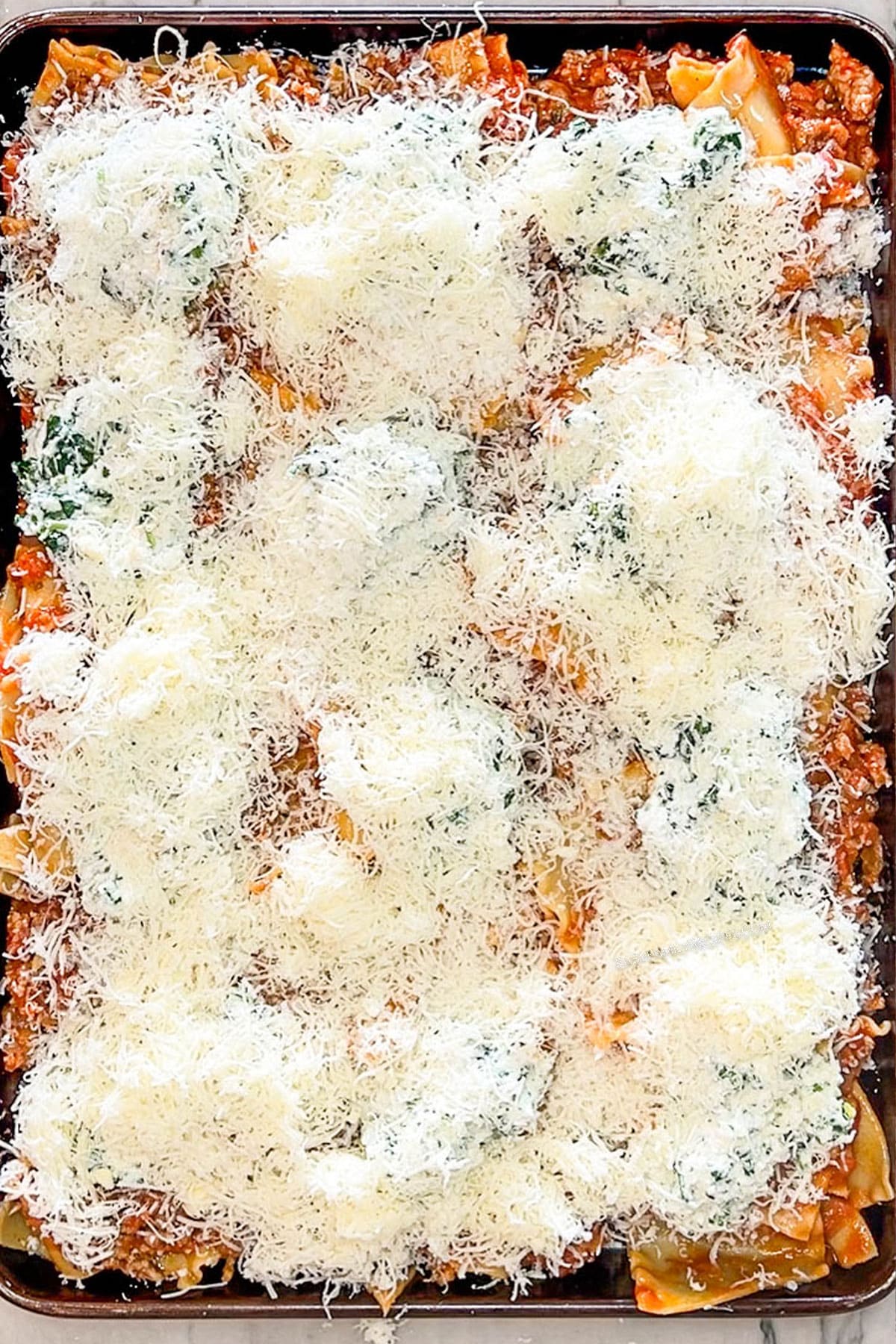 Pan of ground beef and marinara mixture, dollops of ricotta, mozzarella and spinach mixture, topped with shredded parmesan cheese