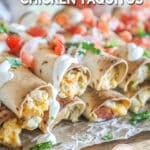 Close up of Baked Chicken Taquitos with toppings including pico and sour cream- on foil and a wooden board