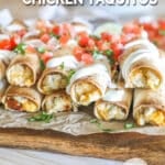 Close up of Baked Chicken Taquitos with toppings including pico and sour cream- on foil and a wooden board with a wooden background