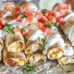 Close up of Baked Chicken Taquitos with toppings including pico and sour cream- sitting on foil
