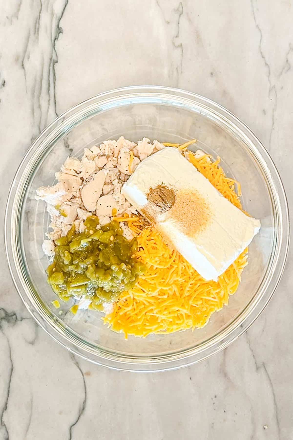 Glass bowl with the ingredients to make Baked Chicken Taquitos. On a marble background