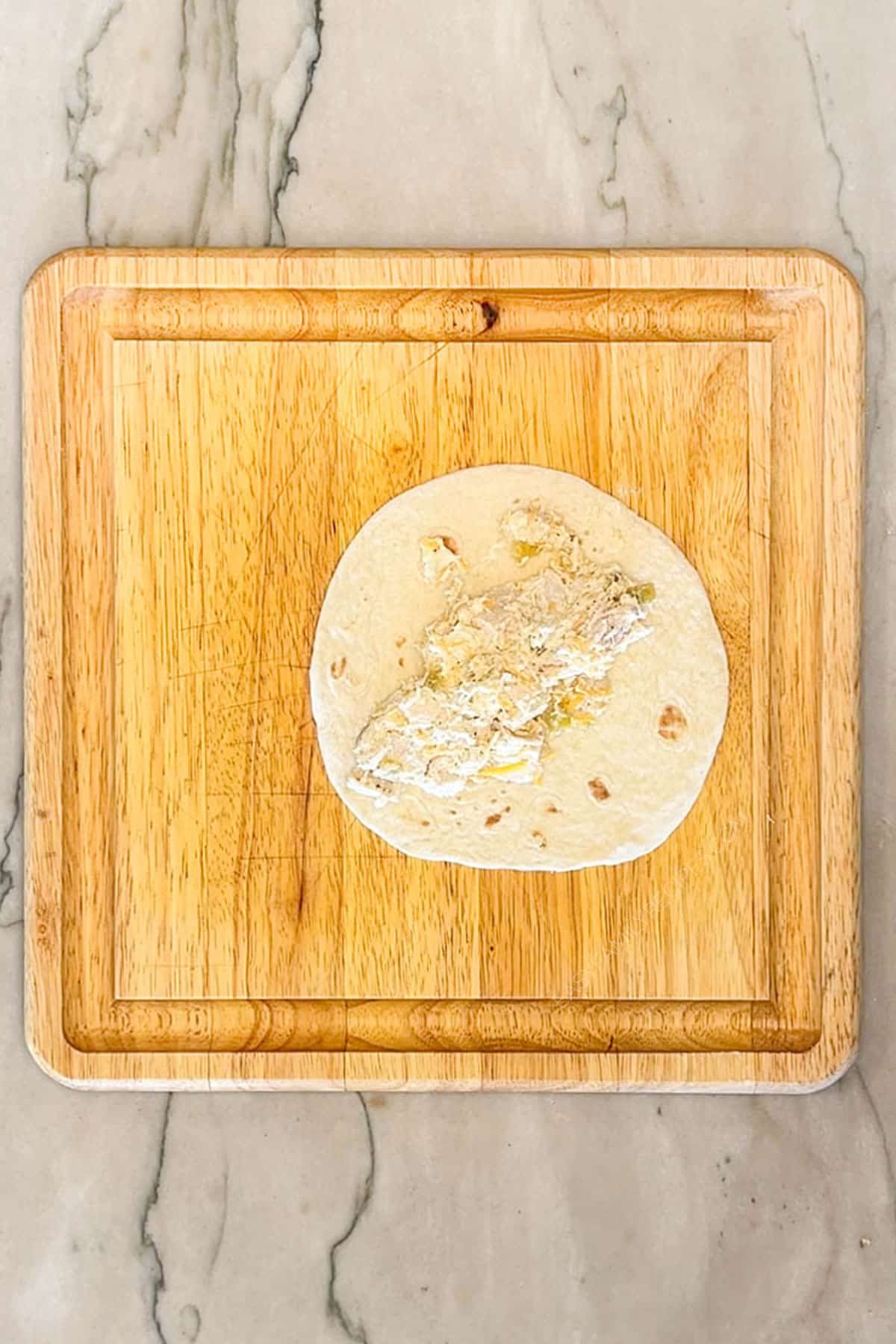 Tortilla with chicken mixture for Baked Chicken Taquitos. On a wooden board with a marble background