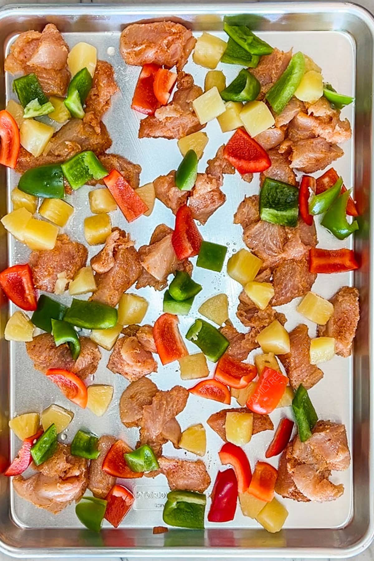 Overhead shot of chicken with vegetables on a sheet pan before cooking.
